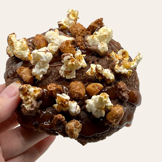 Close-up of The Cinema Crunch Chocolate Cookie from The Dough Corner – a rich quadruple chocolate chip cookie with a creamy peanut butter core, topped with caramel bits and candied peanuts for a perfect blend of flavors and textures. Ideal for movie night treats and chocolate lovers.
